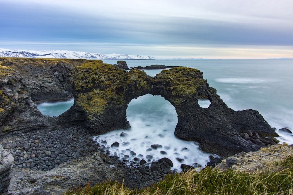 black and brown rock formation on sea under gray sky