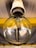 A close-up view of a clear incandescent light bulb mounted on a ceiling. The metal base and the glass bulb are prominently visible, with a slightly reflective surface capturing light and shadows. The internal filament structure of the bulb is apparent, and the fixture appears to be attached to a yellow support structure under a metallic ceiling.