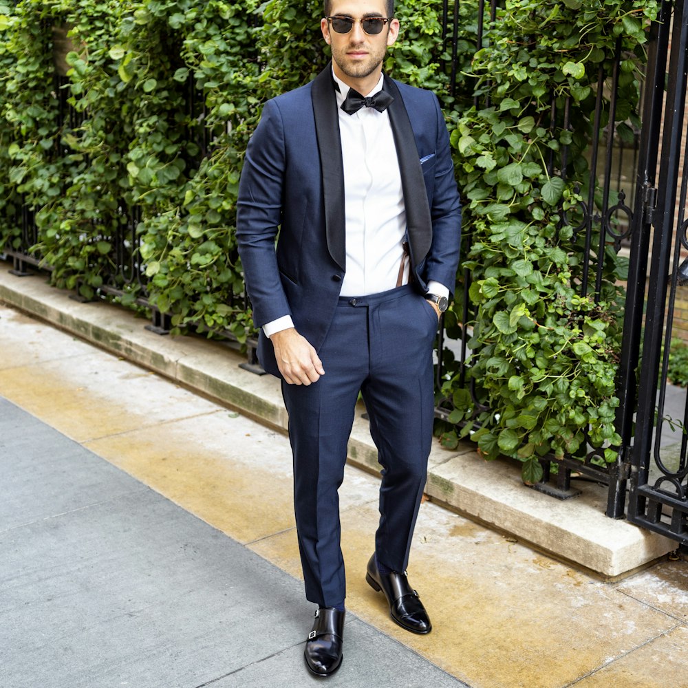 man in black suit standing on sidewalk during daytime