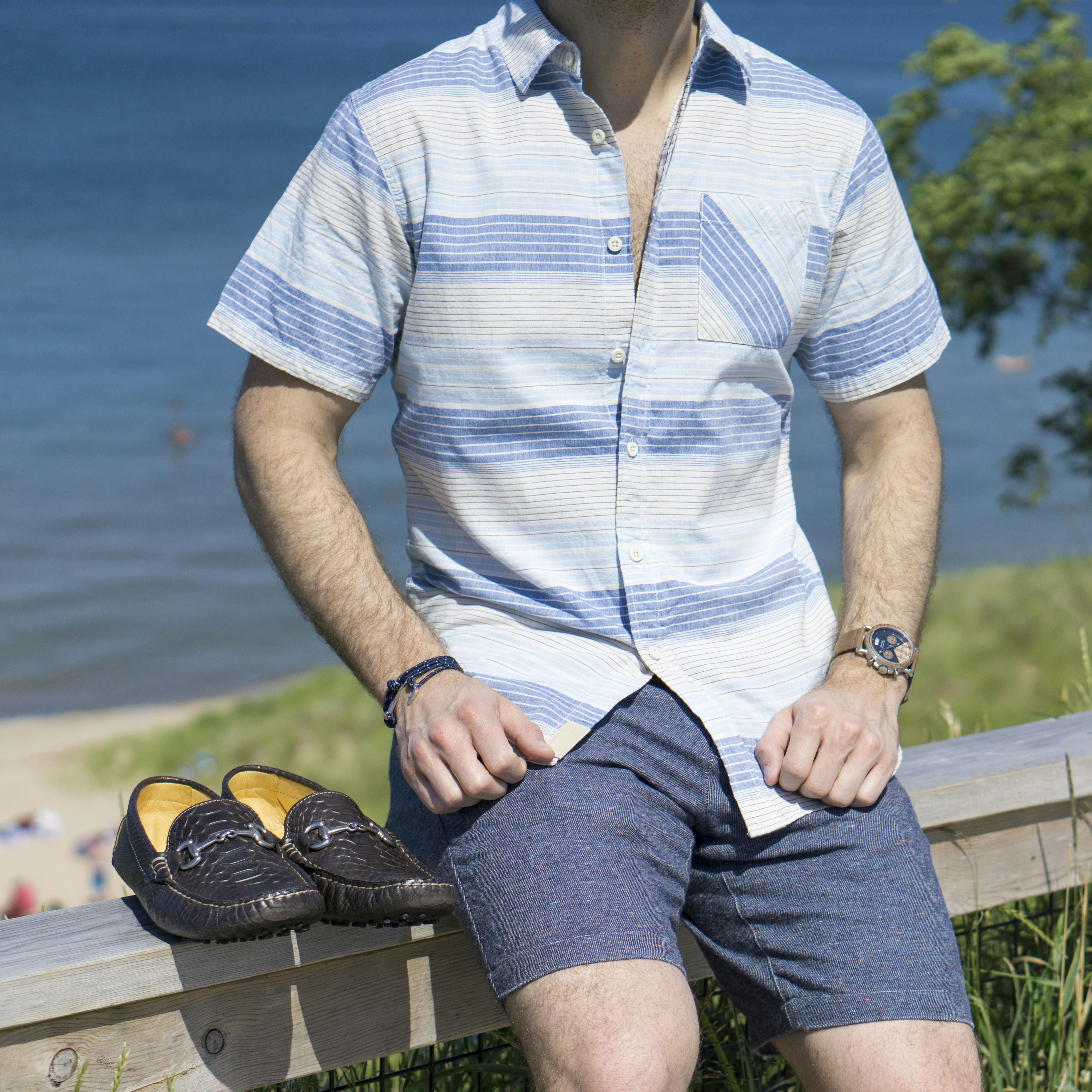 Mann in weißem Button-up-Hemd und schwarzen Shorts sitzt auf Holzbank