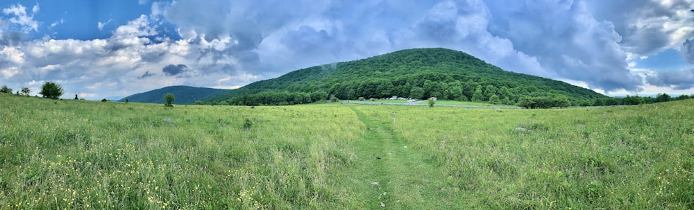 green grass field near green mountain under white clouds and blue sky during daytime