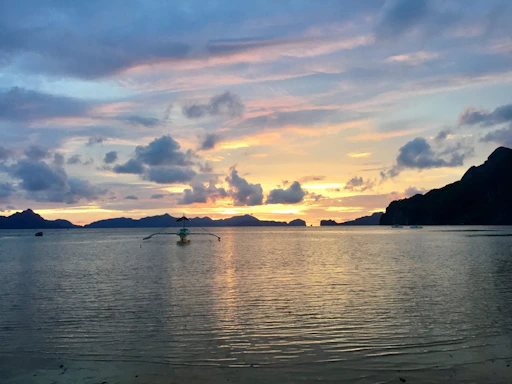 A serene coastal scene with gentle waves and a small boat at sunset.