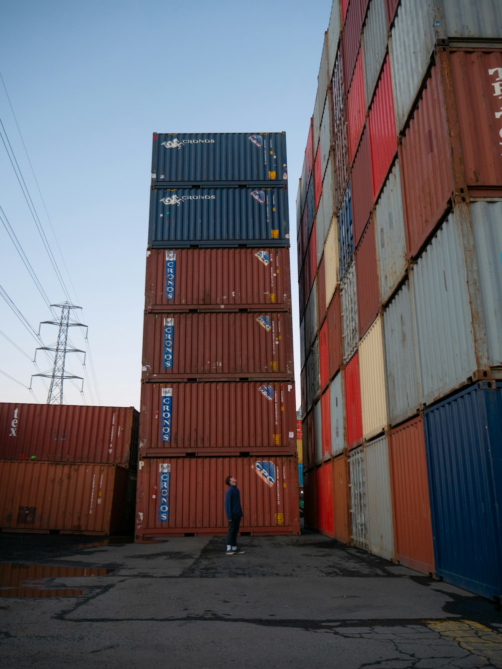 Mann im blauen Hemd geht tagsüber in der Nähe roter Frachtcontainer spazieren