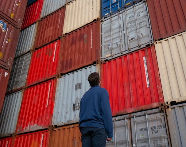 man in blue long sleeve shirt standing in front of red and blue intermodal containers