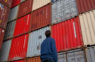 man in blue long sleeve shirt standing in front of red and blue intermodal containers