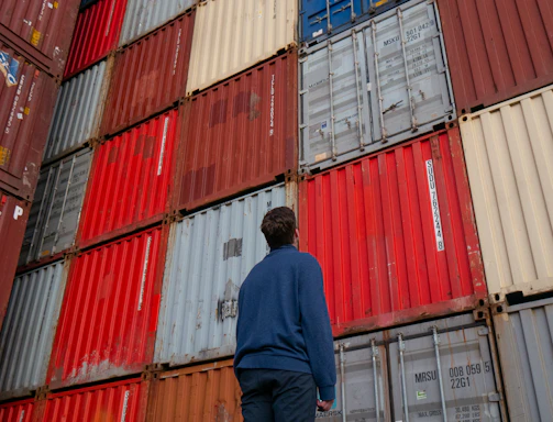 man in blue long sleeve shirt standing in front of red and blue intermodal containers