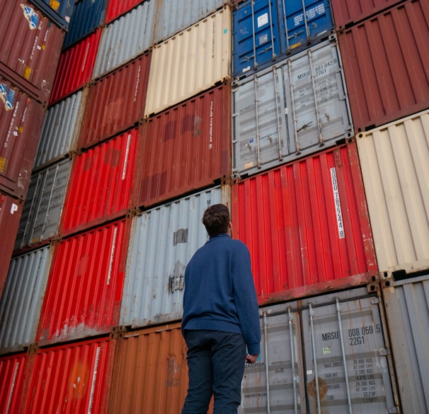 man in blue long sleeve shirt standing in front of red and blue intermodal containers