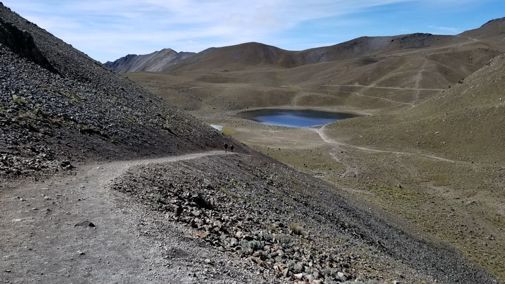 green and brown mountain beside lake under blue sky during daytime