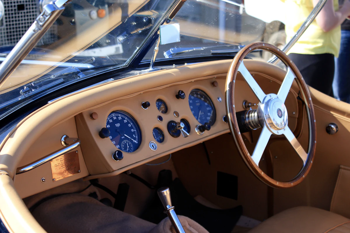 Warm-toned view of a restored classic car cabin showing a wooden dashboard and round gauges