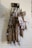 Several cured sausages hang on a wall display, wrapped in netting and secured with tags. The sausages are labeled 'Chorizo' and appear to be part of a specialty meat selection. They are suspended by black hooks against a light-colored brick wall.
