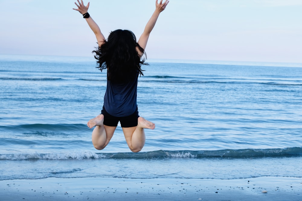 woman in black tank top and black shorts jumping on sea during daytime