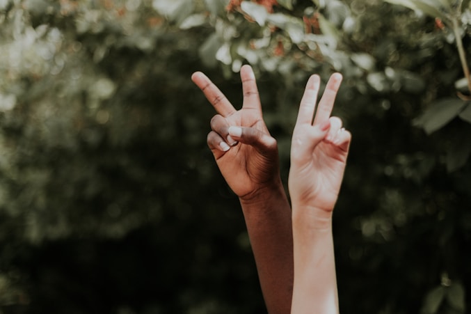 Peace sign gesture by two hands in front of a green background, reflecting grassroots movements 