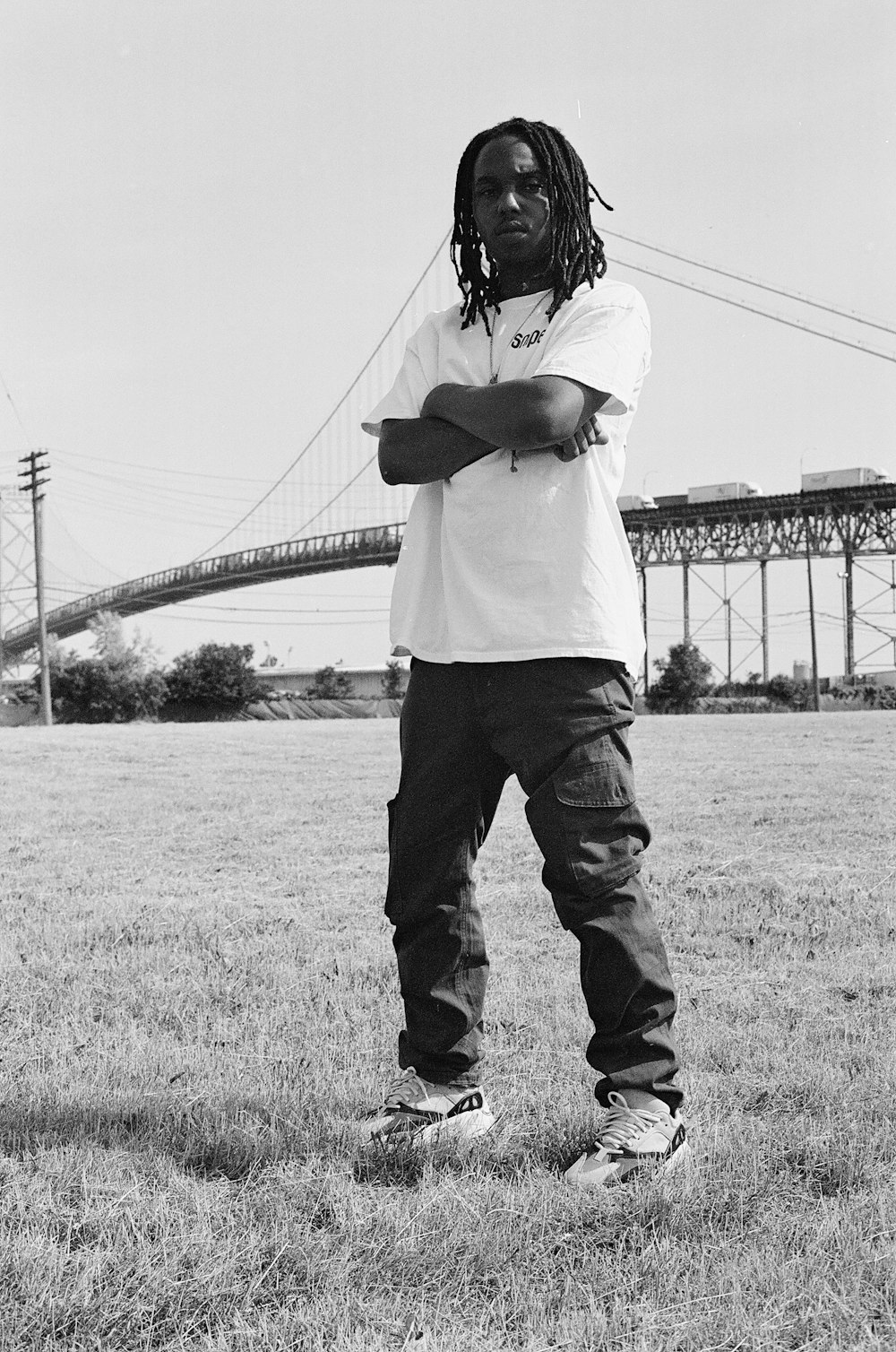 man in white shirt and black pants standing on grass field near bridge