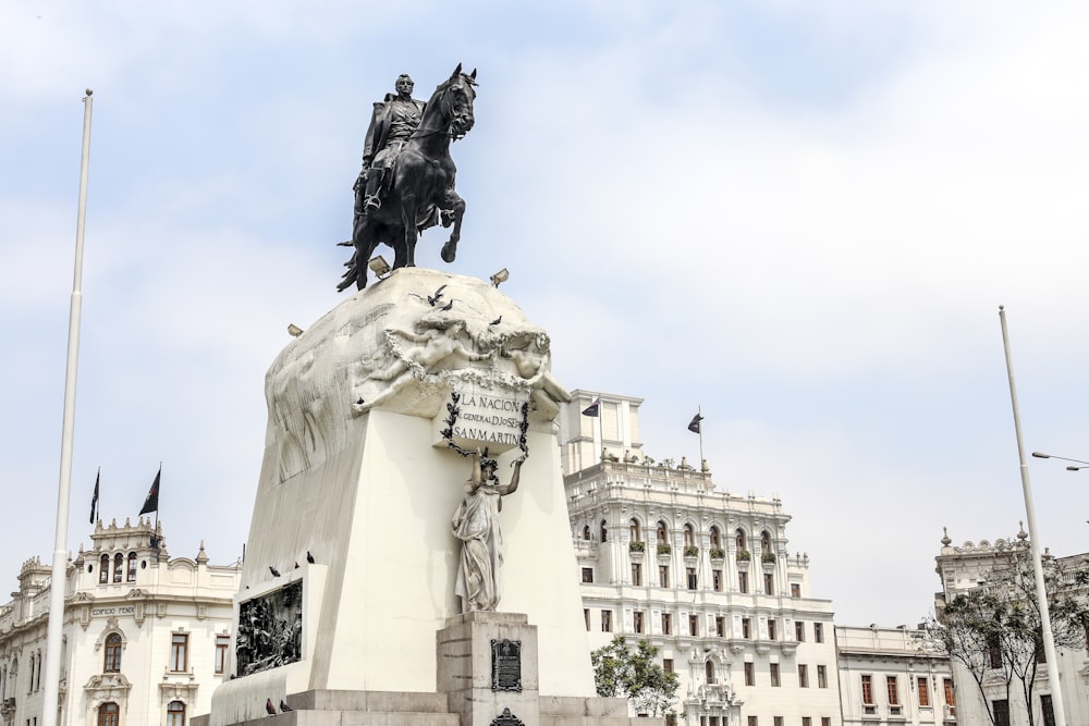 Statua dell'uomo che cavalca il cavallo vicino all'edificio in cemento bianco durante il giorno