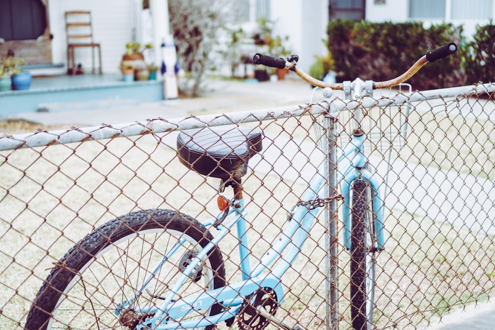 blue and black bicycle leaning on blue metal fence during daytime