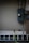 A brick wall painted in a light neutral color has an electrical meter and panel installed on it. A metal ladder is leaning horizontally at the bottom, and a green garden hose is attached to an exterior faucet.