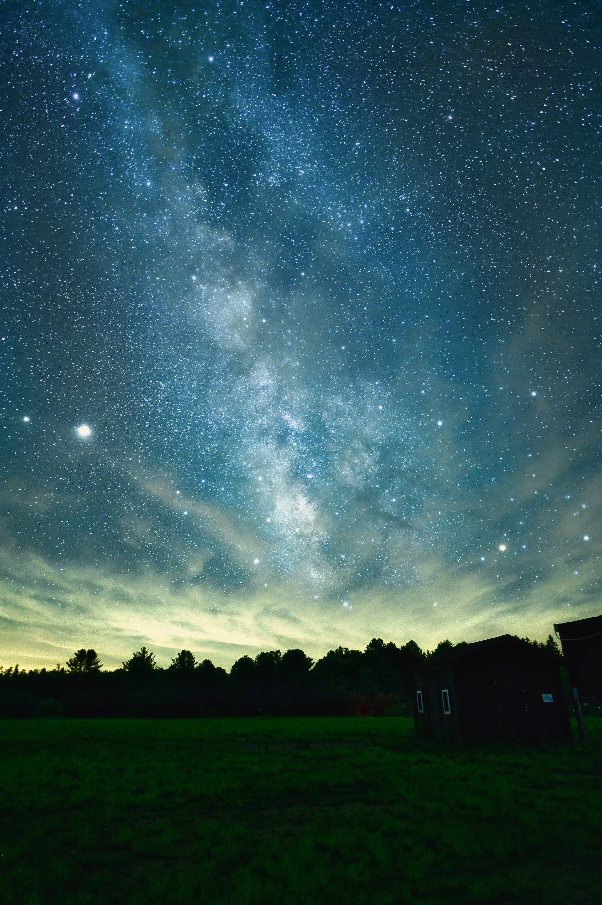 An artistic shot of the Milky Way stretching across the horizon over a quiet landscape.