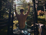 Male calisthenics athlete performing a muscle-up on outdoor bars at sunrise.