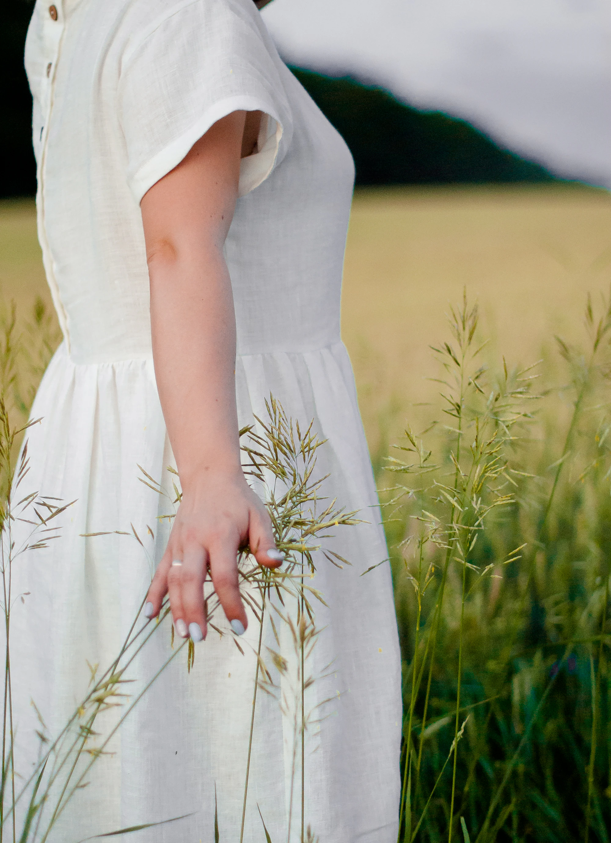 Woman in a white linen dress standing in a sunlit field