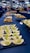 An assortment of small, meticulously arranged appetizers is displayed on a large table. The appetizers include green and white balls in wooden bowls, pastries, and dishes topped with creamy sauces. People in the background are gathered, possibly for an event, with some picking up food items.