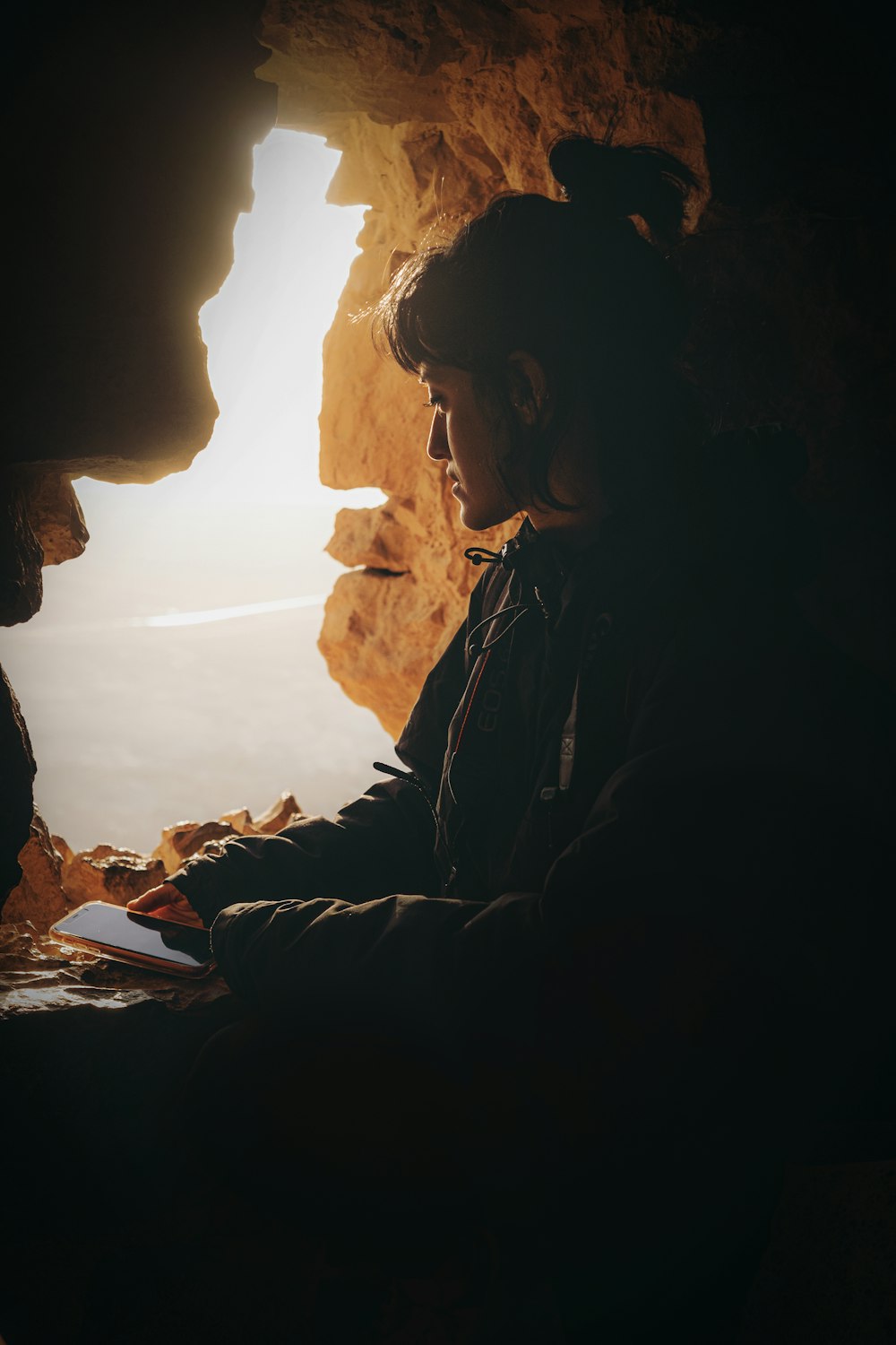 woman in black jacket sitting on rock formation during daytime