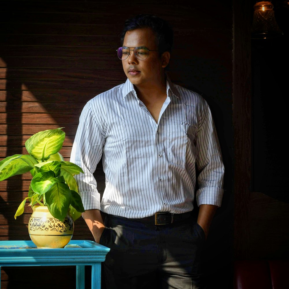 man in white and blue striped dress shirt standing beside green plant