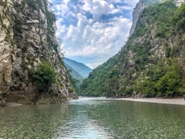 river between green trees and mountains under blue sky and white clouds during daytime