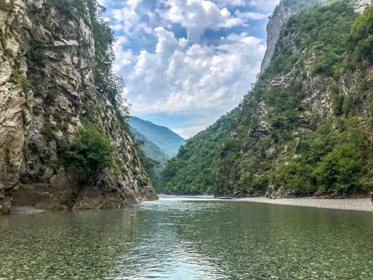 River between green trees and mountains under blue sky and white clouds during daytime — Gjirokastër, Albania