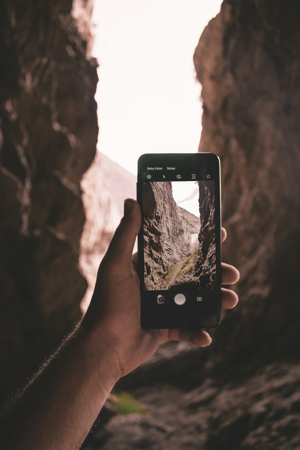 a hand holding a cell phone taking a picture of a mountain