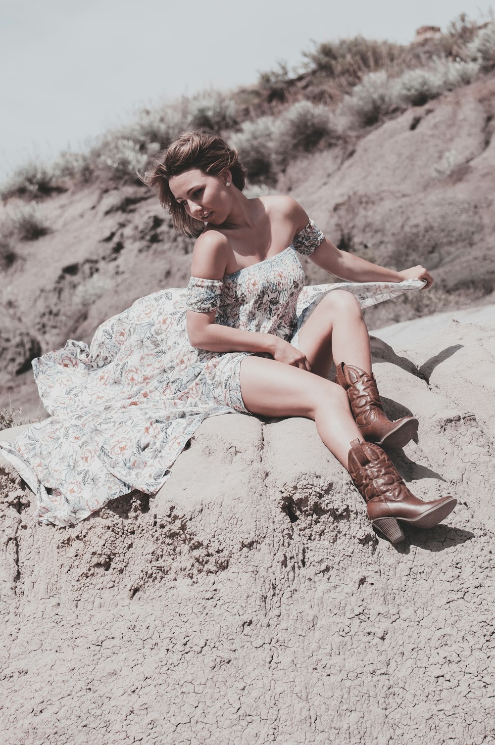 woman in white and blue floral dress sitting on brown sand during daytime