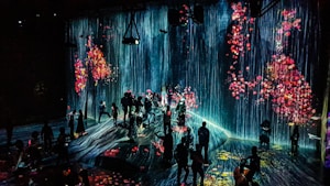 A dark room is filled with people viewing a digital art installation featuring cascading virtual waterfalls against an ethereal backdrop. The artwork is interspersed with vivid floral patterns, creating a vibrant and immersive environment.