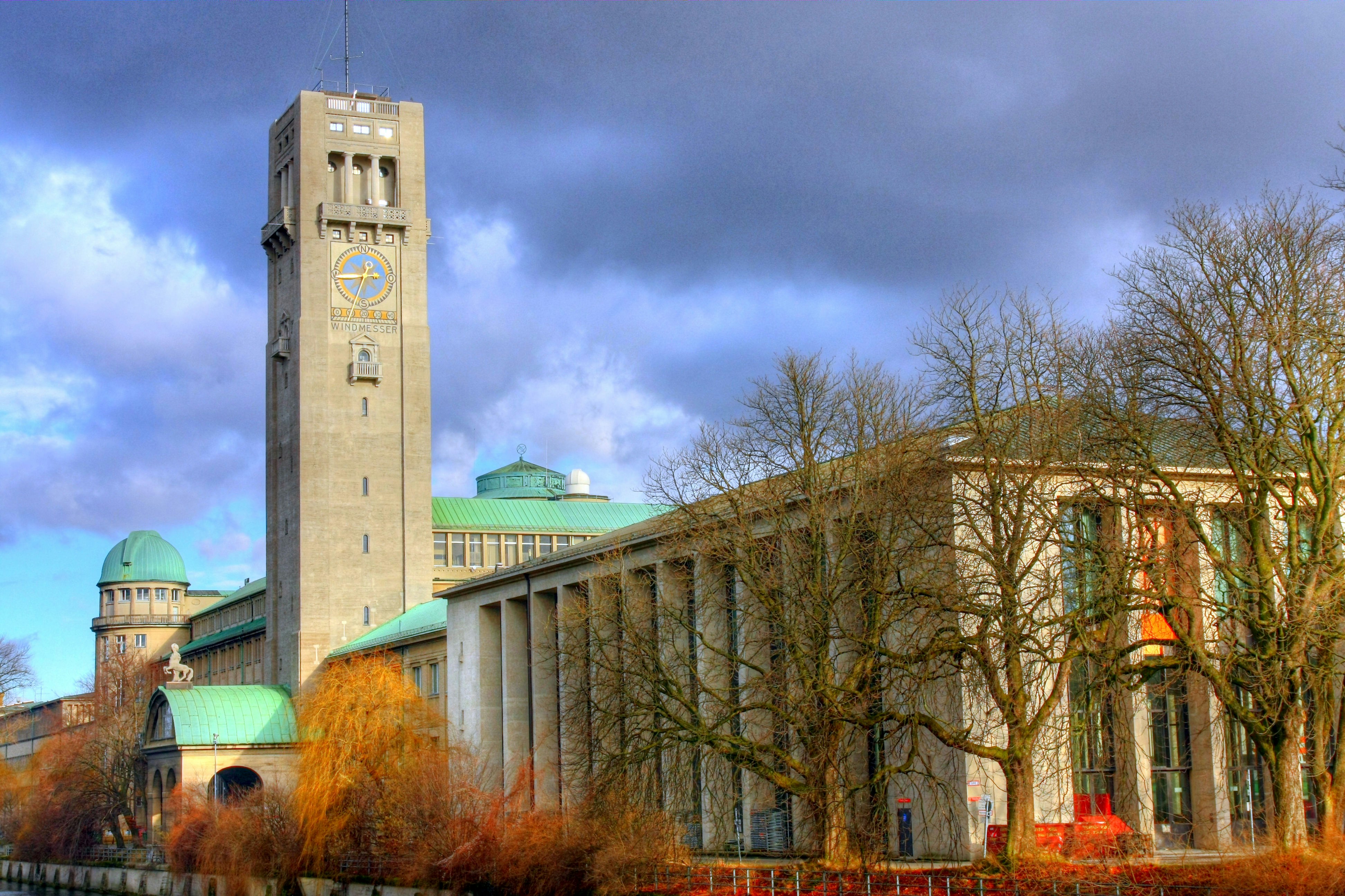 brown concrete building near bare trees under cloudy sky during daytime