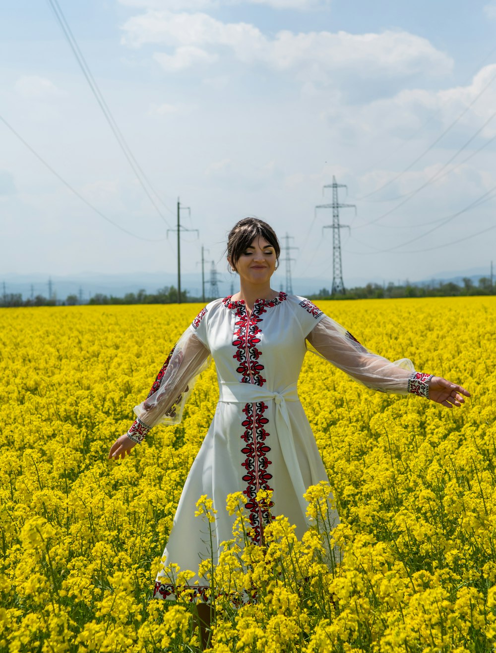 woman in white and red floral dress standing on yellow flower field during daytime