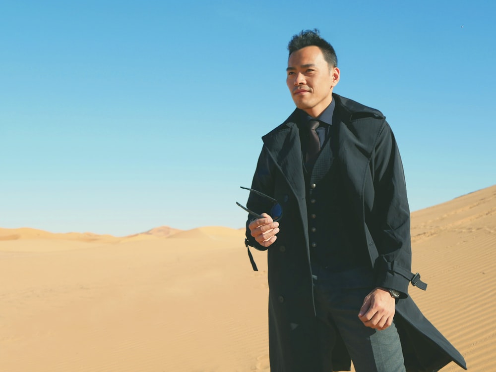 昼間の砂漠に立つ黒いスーツの男