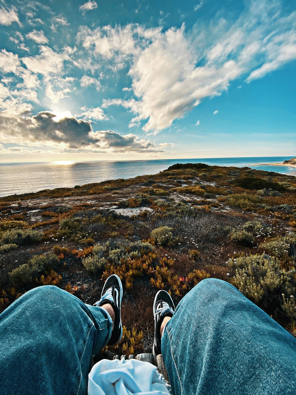 person in blue denim jeans and black and white sneakers sitting on green grass field during