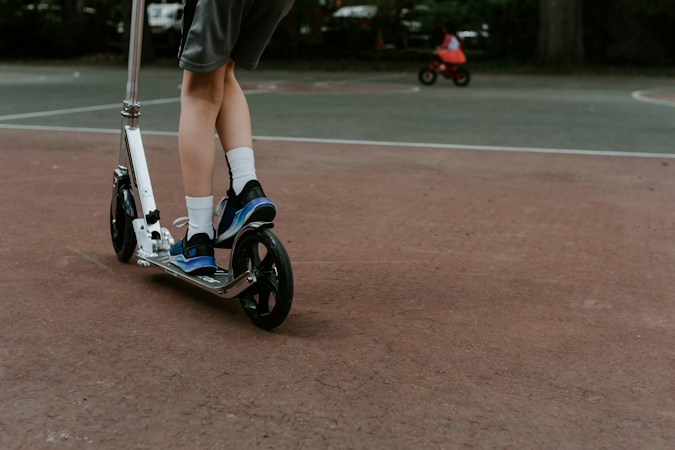 Two riders on kick scooters moving through daytime street traffic