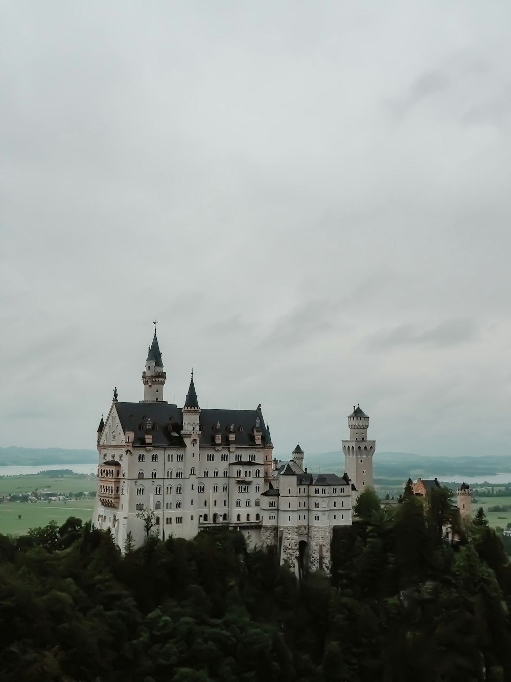 white and black concrete castle near green trees under white clouds during daytime