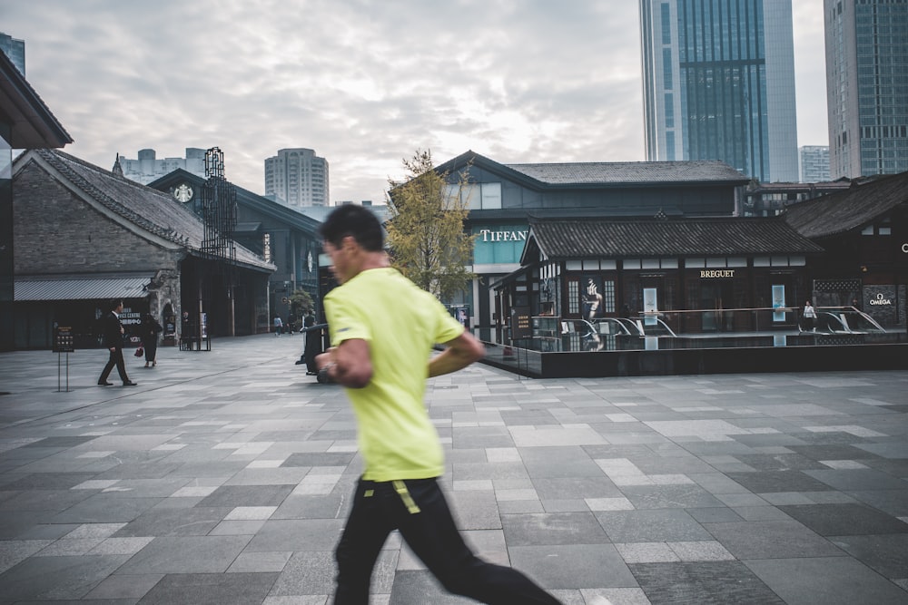 man in green t-shirt and black pants walking on sidewalk during daytime