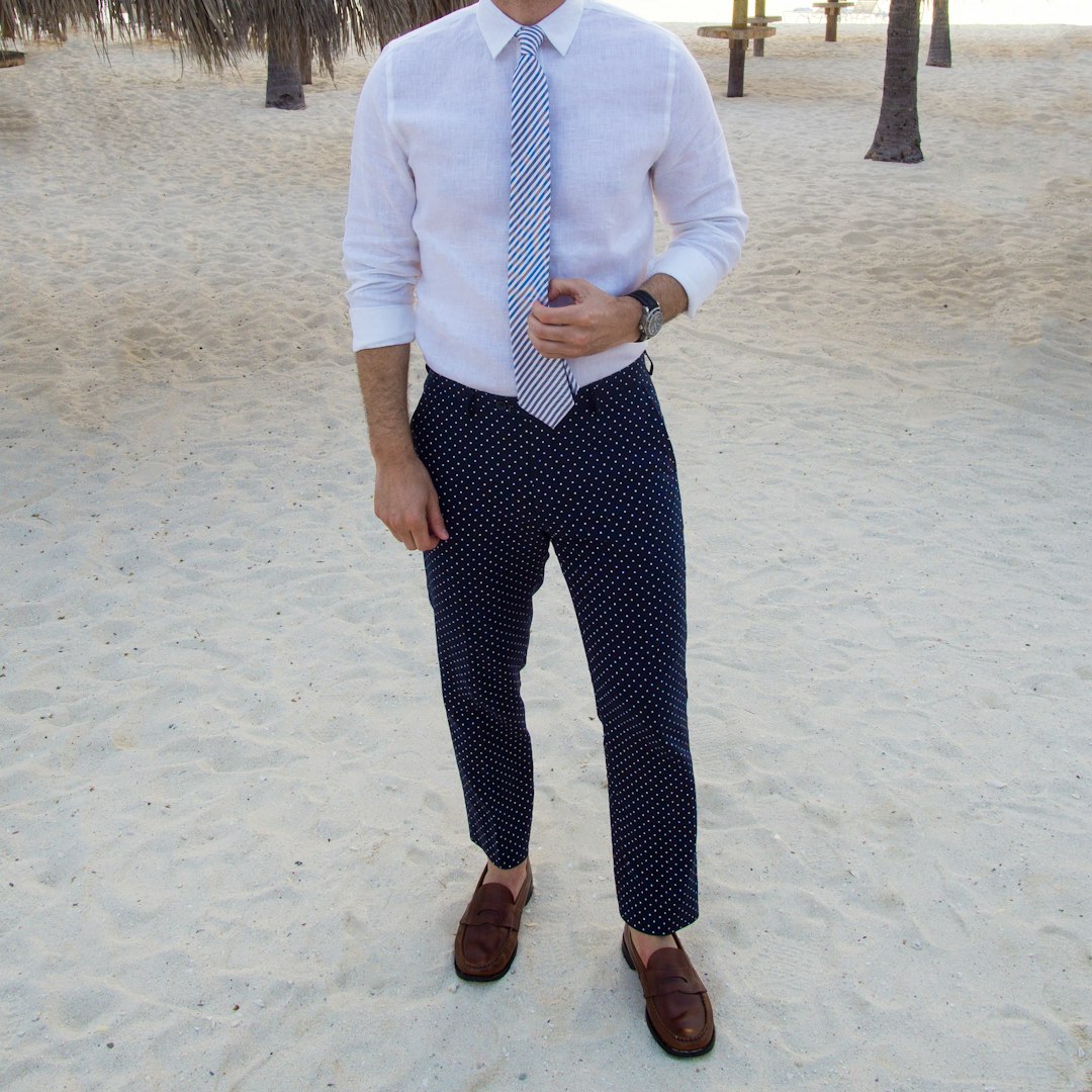 man in white dress shirt and black pants standing on white sand during daytime