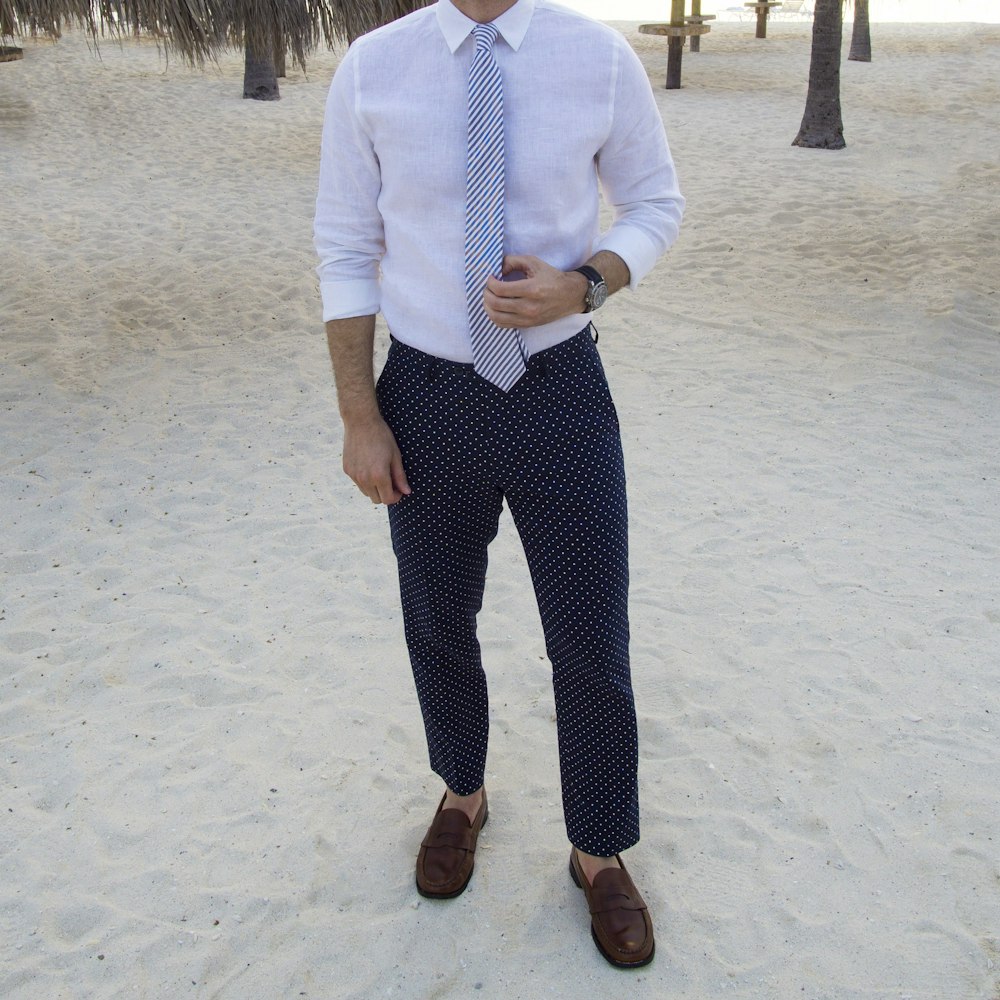 man in white dress shirt and black pants standing on white sand during daytime