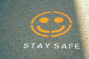 An orange spray-painted smiley face and the text STAY SAFE on grey asphalt