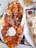 A platter filled with various types of grilled meats including chicken and lamb, accompanied by a scoop of rice, slices of flatbread, and vegetables. There is a separate plate with hummus and a portion of flatbread on the side.