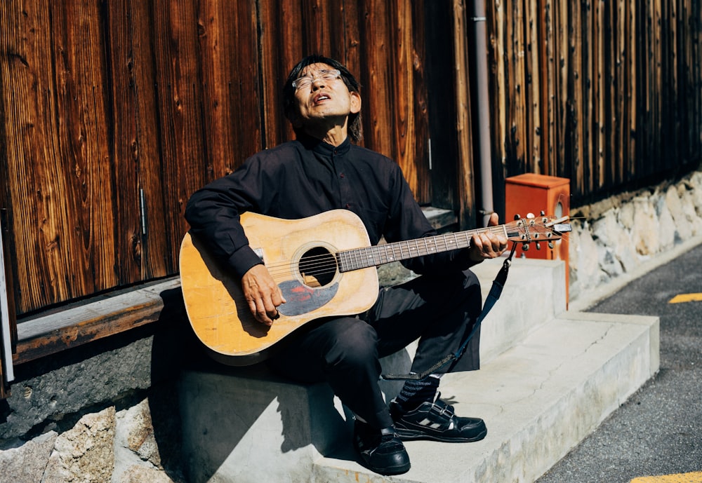 man in black long sleeve shirt playing brown acoustic guitar