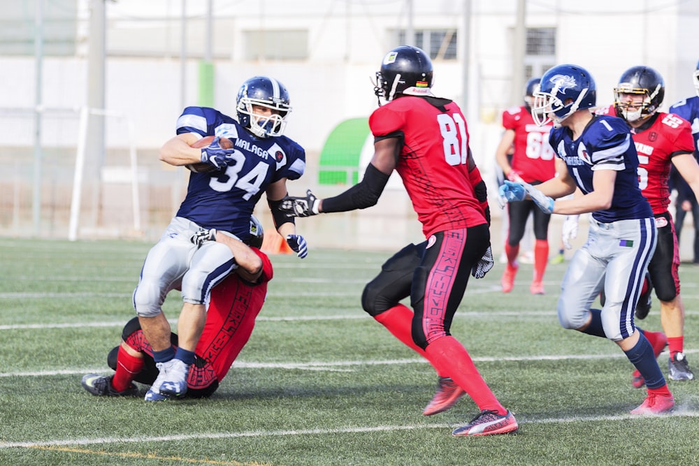 football players in red jersey shirt and red pants running on green grass field during daytime