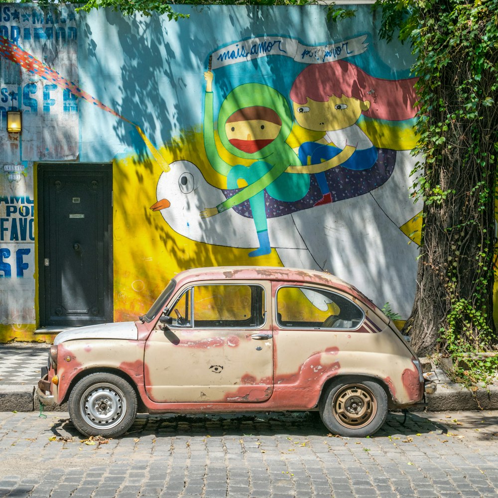 pink sedan parked beside wall with graffiti