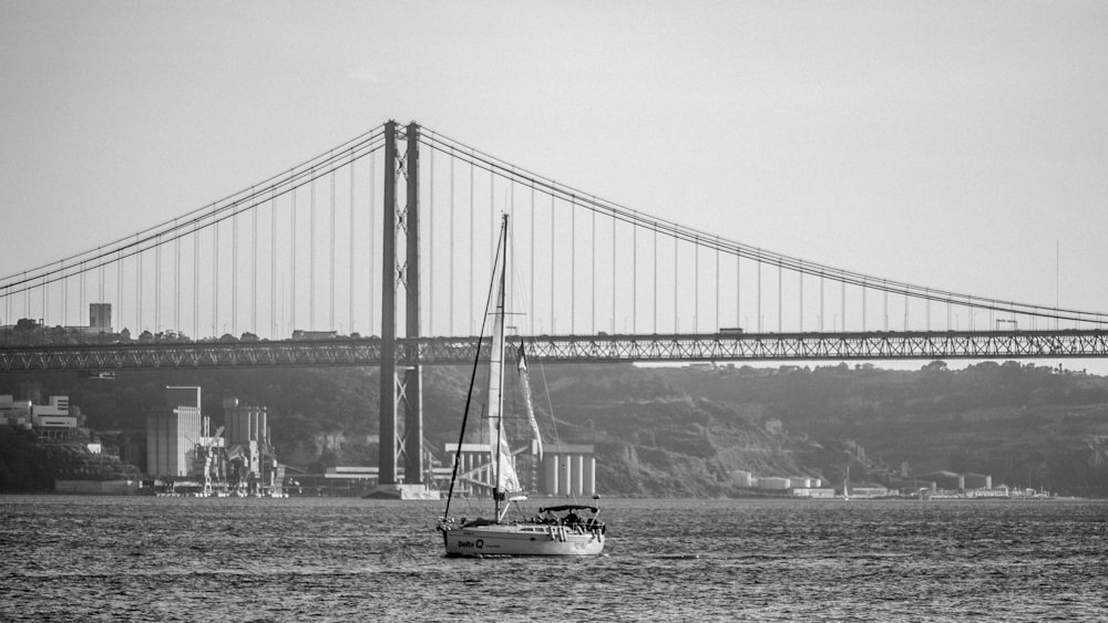 grayscale photo of boat on sea near bridge