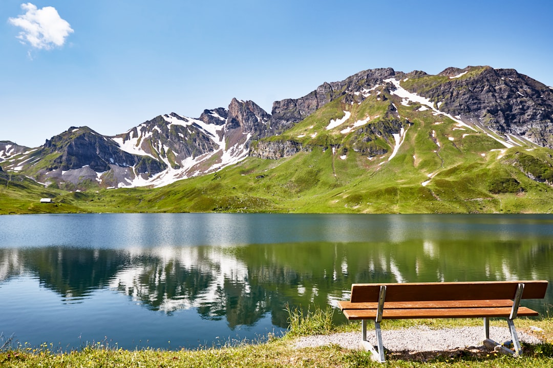 brown wooden bench on snow covered ground near lake and mountains during daytime