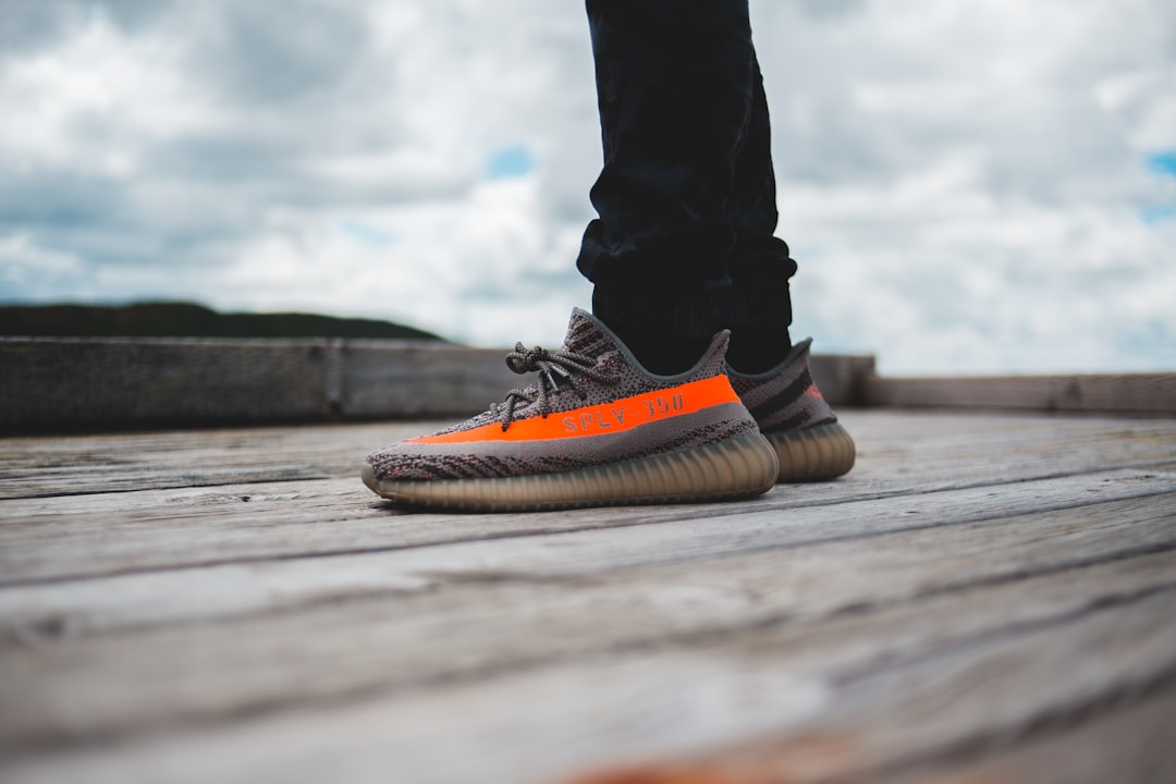 person in blue denim jeans and black and orange nike sneakers standing on brown wooden dock