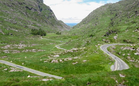 gray asphalt road between green grass covered mountains during daytime in Gap of Dunloe Ireland