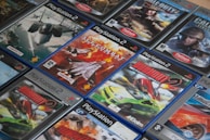 A collection of PlayStation 2 video game cases arranged closely together, featuring titles such as Ace Combat and Burnout. The cases display a mix of action and racing game covers, with vibrant images of fighter jets and cars.